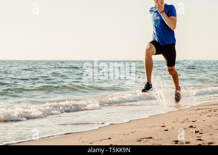 Männliche Läufer, die auf Meer Strand Wasser sprühen Stockfoto
