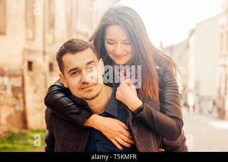 Junger Mann, der piggyback Ride zu seiner Freundin. Glückliches Paar in der Straße. In warmen Farbtönen. Stockfoto