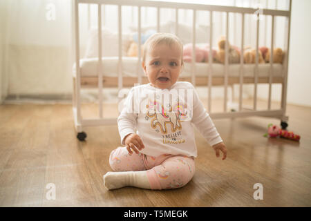 Ein trauriges Kind sitzt auf dem Boden und schreit vor Hintergrund der Krippe. Stockfoto