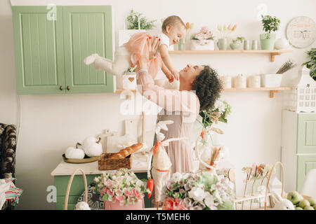 Glückliche Mutter spielt mit ihrem Baby in der Küche auf dem Hintergrund von Ostern Dekorationen. Stockfoto