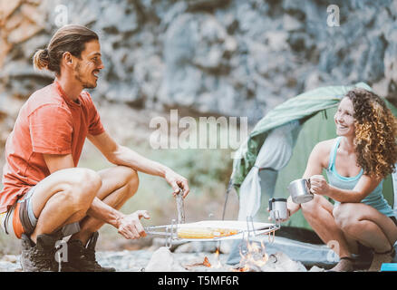 Trekker paar Camping in Rock Berge mit einem Zelt Bergsteiger Menschen kochen und trinken heißen Tee neben Lagerfeuer Stockfoto