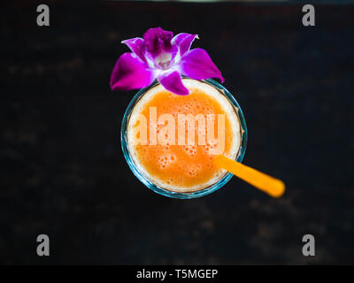 Frisch multi Frucht orange Smoothie aus verschiedenen tropischen Früchten in ein Becherglas mit einer Orchidee auf einem dunklen Hintergrund eingerichtet. Stockfoto