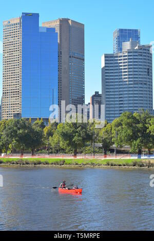 Erwachsene und Kinder Paddeln in rot Kanu in Yarra River in Melbourne an einem sonnigen Tag mit Wolkenkratzern im Hintergrund. Stockfoto