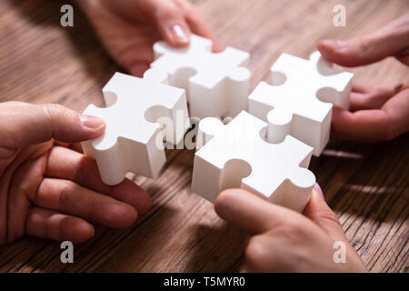 In der Nähe von Geschäftsleuten weiß Puzzle zusammen Lösen auf hölzernen Schreibtisch Stockfoto