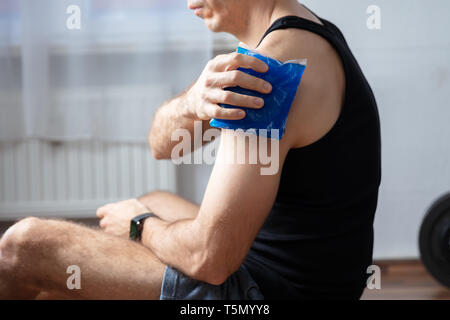 Nahaufnahme der männlichen Trainer Anwendung Cool Gel Pack auf seine verletzte Schulter im Fitnessstudio Stockfoto