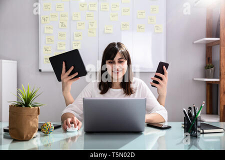 Lächelnden jungen Geschäftsfrau zu tun Multitasking am Arbeitsplatz Stockfoto