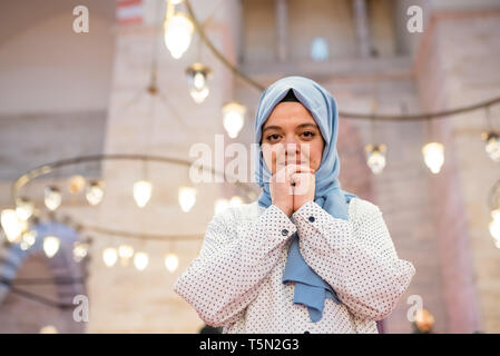 Muslimische Frau in Kopftuch und Hijab betet, während ihre Hände umklammern mit Moschee auf Hintergrund. Religion beten Konzept. Stockfoto