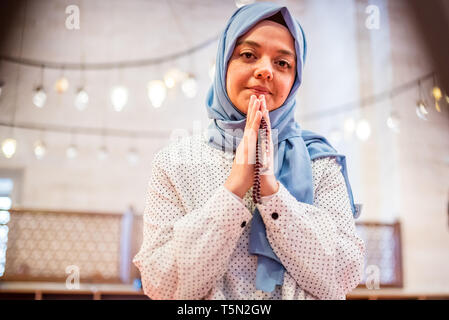 Muslimische Frau in Kopftuch und Hijab betet, während ihre Hände umklammern mit Moschee auf Hintergrund. Religion beten Konzept. Stockfoto