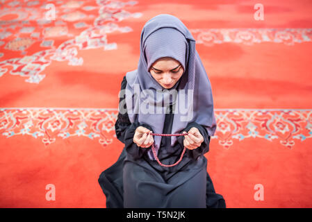 Muslimische Frau in Kopftuch und Hijab betet mit den Händen in der Luft halten Rosenkranz in Moschee. Religion beten Konzept. Stockfoto