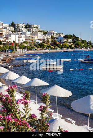 Weißen Sonnenschirmen und Liegen in der Nähe der Lagune mit Booten auf dem Strand in Bodrum, Türkei Stockfoto