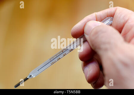 Ein Mann hält eine Quecksilber Fieberthermometer in seiner Hand. Stockfoto