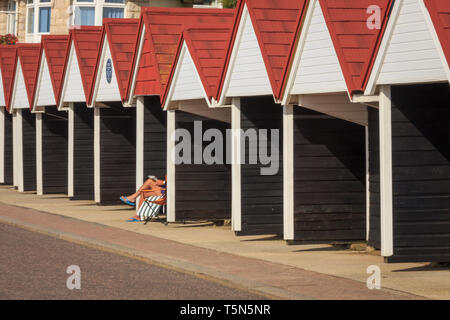Strand Hütten auf bouremouth am Meer mit Darlehen Sonnenanbeter im Stuhl sitzen. Dorset England Stockfoto