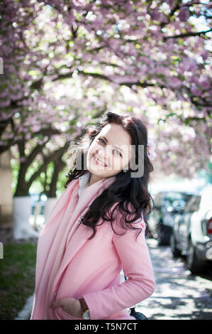 Mädchen in rosa Kleidung mit Sakura Blume im Haar posing unter dem Kirschbaum Stockfoto