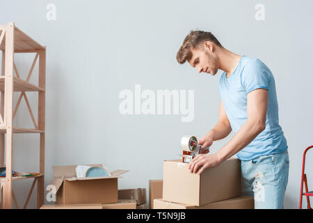 Jungen blonden Mann, der seinen neuen Platz, der Holding scoth Tape tool Verpackung Karton lächelnd Denken der Verlagerung Stockfoto