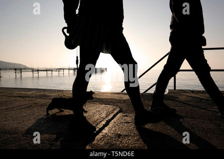 Spaziergang mit dem Hund entlang der Promenade Verkleidung Gehweg zwischen Totland und Colwell Buchten. Zwei Wanderer in Silhouette mit einer untergehenden Sonne über Totland Pier. Stockfoto