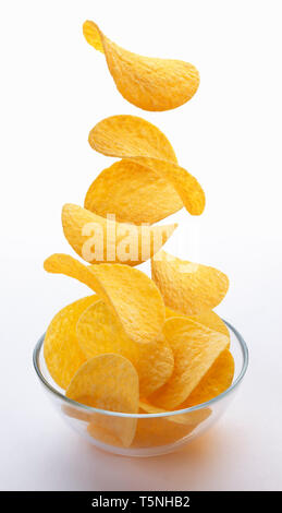 Kartoffel Chips fallen in Glasschale auf weißem Hintergrund, fliegende Kartoffelchips Stockfoto