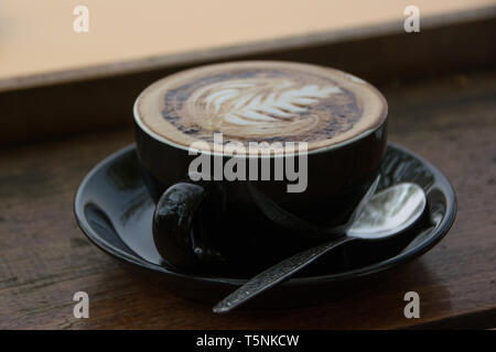 Schöner Cappuccino in einer schwarzen Tasse mit Blick auf den Mekong in Luang Prabang, Laos. Stockfoto