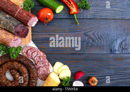Viele Arten von Wurst, geräucherter Käse, frisches Gemüse auf einem hölzernen Hintergrund. Produkte in den Urlaub. Kopieren Sie Platz. Ansicht von oben. Flach. Stockfoto
