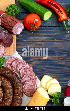 Viele Arten von Wurst, geräucherter Käse, frisches Gemüse auf einem hölzernen Hintergrund. Produkte in den Urlaub. Kopieren Sie Platz. Ansicht von oben. Flach. Stockfoto