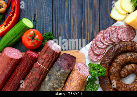 Viele Arten von Wurst, geräucherter Käse, frisches Gemüse auf einem hölzernen Hintergrund. Produkte in den Urlaub. Kopieren Sie Platz. Ansicht von oben. Flach. Stockfoto