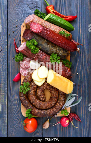 Viele Arten von Wurst, geräucherter Käse, frisches Gemüse auf einem hölzernen Hintergrund. Produkte in den Urlaub. Ansicht von oben. Flach. Stockfoto
