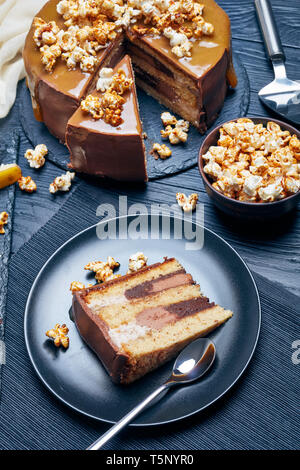 Bananenscheiben Biskuitteig, überlagert mit Peanut butter Mousse und gekrönt mit Ganache, geschmolzen, Karamell und süßes Popcorn, vertikale Ansicht von ab Stockfoto