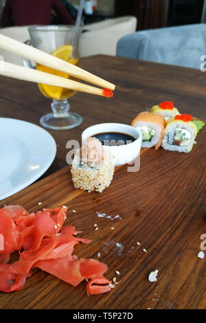 Der Mensch isst Sushi in die schwarze Platte auf einem Holztisch, Brötchen close-up 2019. Stockfoto