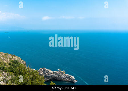 Blick auf das wunderschöne blaue Meer von einer Klippe, Amalfi Küste. Sichtbare Bucht und die Ruinen einer kleinen Burg auf dem Felsen. Schiffe segeln in der Ferne Stockfoto