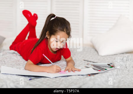 Süßes kleines Kind Mädchen in roten Schlafanzug zieht mit Bleistift zu Hause Stockfoto