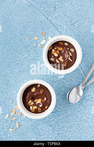 Dunkle Schokolade Dessert in zwei keramische Förmchen und Löffel auf Blau texturiert und gemusterten Hintergrund. Ansicht von oben und Platz für Text. Stockfoto