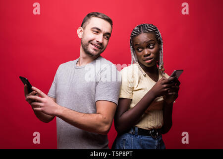 Glückliches Paar Sms vom Handy Seite an Seite auf rotem Hintergrund Stockfoto