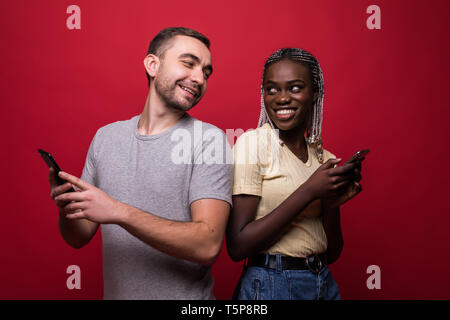 Glückliches Paar Sms vom Handy Seite an Seite auf rotem Hintergrund Stockfoto