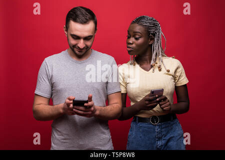 Portrait von gemischten Rennen Mann und Frau runzelte die Stirn und spähen an jeden anderen Handys über den roten Hintergrund Stockfoto