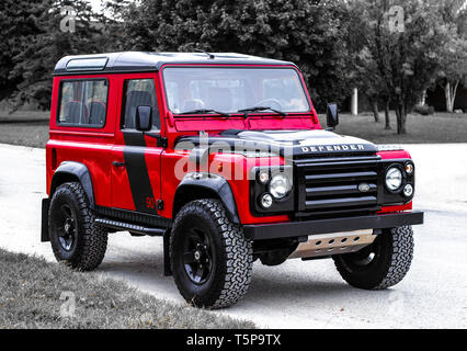 Ein roter Klassiker Land Rover Defender gegen eine Defokussierten Schwarz und Weiß Natur Pfad Hintergrund Stockfoto