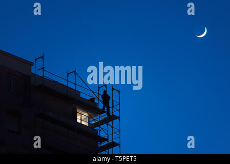 Silhouette der Mann bei der Arbeit hoch oben auf einem Wolkenkratzer Gerüst bei Dämmerung, gefährliche Arbeit, Sicherheit am Arbeitsplatz, blauer Himmel mit Mond im Hintergrund Stockfoto