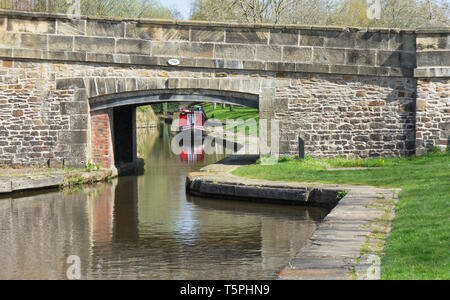 Ein Blick auf einen Kanal und unter einem alten steinernen Brücke in Llangollen Wharf, Wales, mit einem roten 15-04 bis günstig auf der anderen Seite komplett mit reflecti Stockfoto