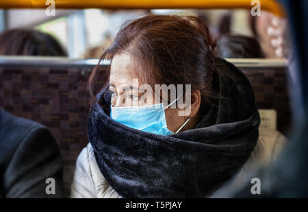 Ältere asiatische Frau mit schwarzen Pelz Schal und chirurgische Verschmutzung Maske sitzt auf einem Bus Zug der U-Bahn Stockfoto