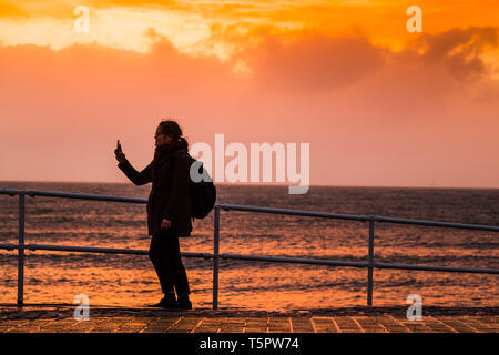 Aberystwyth Wales UK, Freitag, 26. April 2019 UK Wetter: eine Frau nimmt eine selfie an der Küste als Sturm Hannah, die neuesten Tropensturm der Saison 2019 beginnt zu Teig Aberystwyth. Mit den Winden, erwartend, zwischen 60 und 70 mph über Nacht zu Gust, besteht die Gefahr von Sachschäden und Verletzungen. Das Met Office hat eine gelbe Warnmeldung für starke Winde, die viel von der Süden, wenn Großbritannien von heute abend bis Mitte Nachmittag morgen Foto: Keith Morris/Alamy Live Neuigkeiten Stockfoto