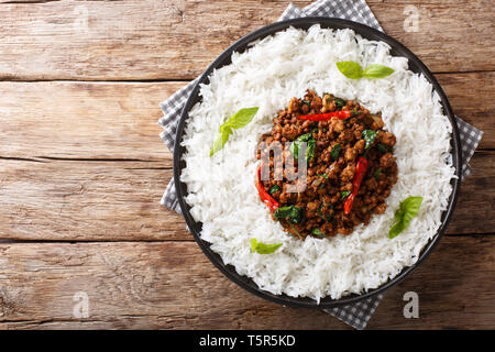 Thai basil Huhn mit pikanter Chili Pfeffer und Sojasauce mit garnieren Reis close-up auf einem Teller auf den Tisch. horizontal oben Ansicht von oben Stockfoto