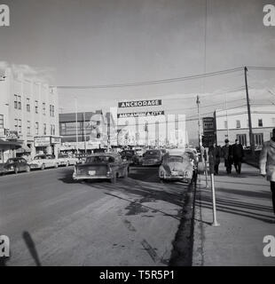 1950, historische, breite Straße in Anchorage, Alaska, mit Autos und Menschen, mit einem Schild mit der Aufschrift 'Amerika', Anchorage, USA. Stockfoto