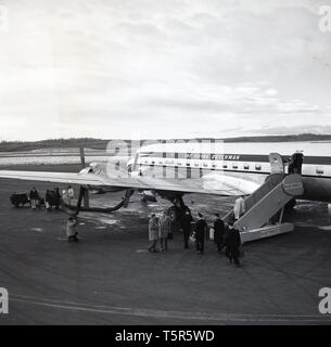 1960, historische, Flughafen Anchorage, Alaska, USA, Passagiere, Piloten und Bodenpersonal in der KLM Einsteigen ins Flugzeug, "Der Fliegende Holländer", geparkt und auf der Start- und Landebahn gewartet. Stockfoto