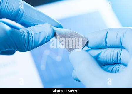 Wissenschaftler Hand in Handschuhe halten und kleine graue poröse Schaumstoff biegen, neue Art von Materialien mit unterschiedlichen Eigenschaften Forschung Konzept Stockfoto