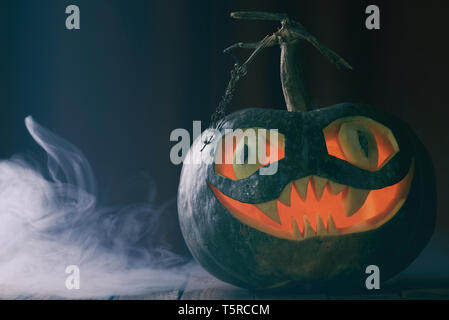 Halloween Kürbis mit lächelnden Gesicht auf Holztisch mit Spooky Blue Mist vintage Farbe getonte geschnitzt Stockfoto