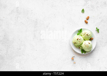 Grüne Eis am weißen Stein Hintergrund, Ansicht von oben, kopieren. Grüne Pistazien, Avocado oder grüner Tee gelato mit Mandeln und Minzeblättchen. Stockfoto