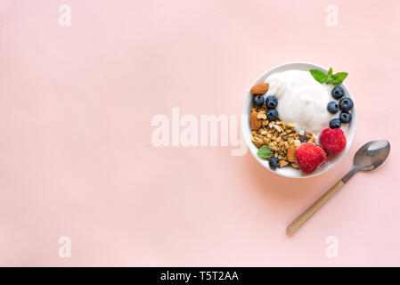 Griechischer Joghurt mit hausgemachtem Müsli und Beeren für gesundes Frühstück auf Rosa pastell Hintergrund, Ansicht von oben, kopieren. Stockfoto