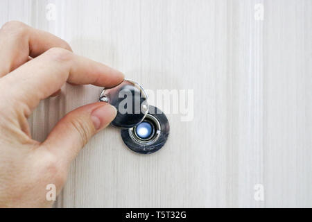 Die Hand öffnet die Tür Guckloch in der Tür von Eiche hell. Stockfoto