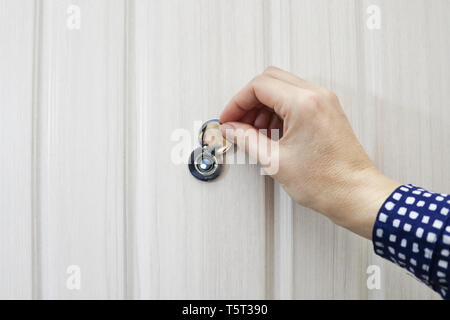 Die Hand öffnet die Tür Guckloch in der Tür von Eiche hell. Stockfoto
