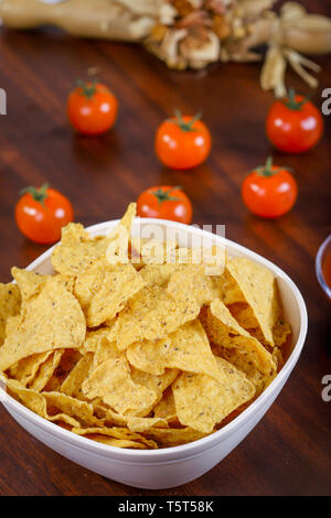 Gelbe nacho in Weiß Schüssel auf den Holztisch mit Tomaten. Stockfoto