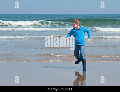 Junge läuft weg von Wellen am Sandstrand. Reise zum Meer genießen. Stockfoto