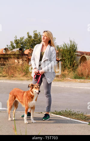 Frau in Spaziergang mit seinem Shetland sheepdog Hund an der Leine. Dog Walker stehen, vor der Kamera posieren. Portrait von Eigentümer und Rough Collie schön. Stockfoto